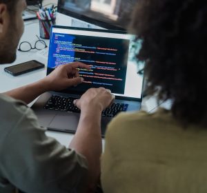 Two adults collaborating on programming tasks using a laptop in an office setting.
